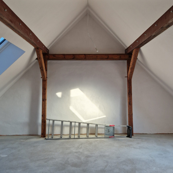 Innenausbau Dachgeschoss Atelier. Sichtbar gelassene Holzbalken der Dachkonstruktion, dunkel lasiert. Seitlicher Lichteinfall durch Dachflächenfenster
