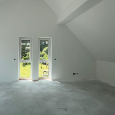 leerer Raum mit Ausblick in den Garten. Weiße Wände, Bodenbelag fehlt noch. Estrich sichtbar